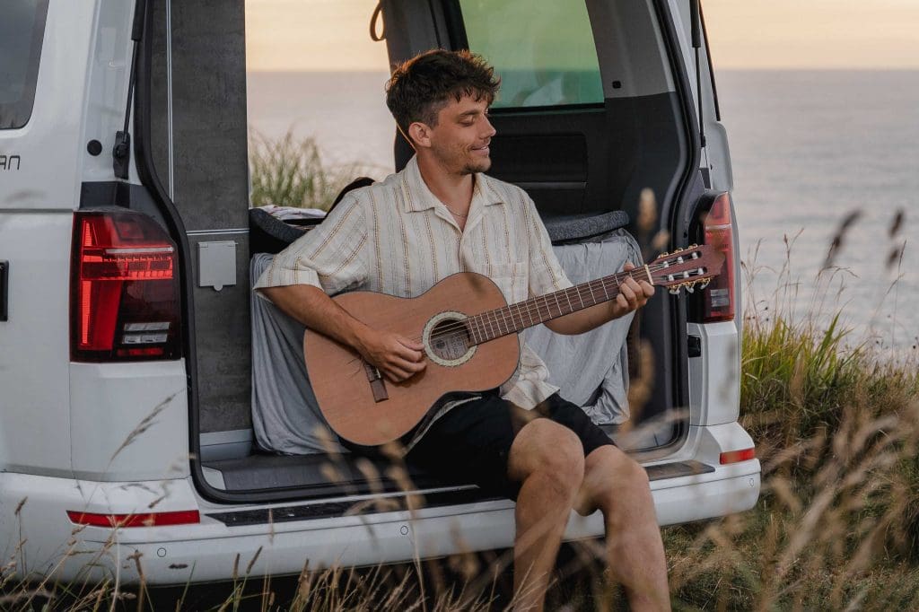 Mann spielt Gitarre im Heck des Campers