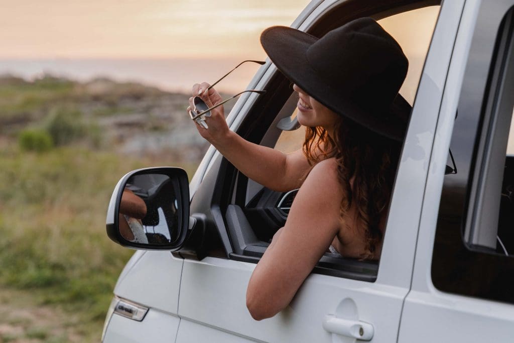 Frau schaut aus Fahrerfenster eine VW California Campers