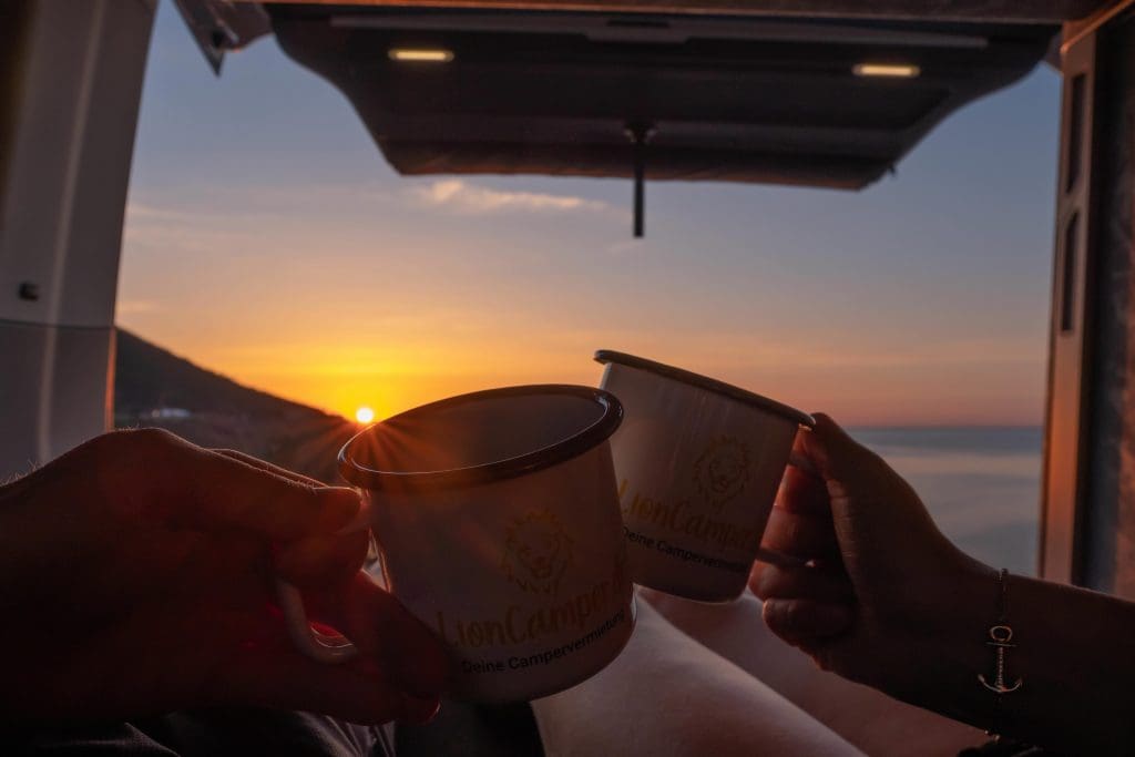 Foto eines Sonnenuntergangs aus dem Camper mit Tassen in der Hand